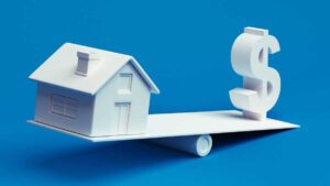 Symbol pieniądza i domu na równoważni. Lepiej inwestować w nieruchomości czy w inwestycje pasywne zgodne z indeksem?