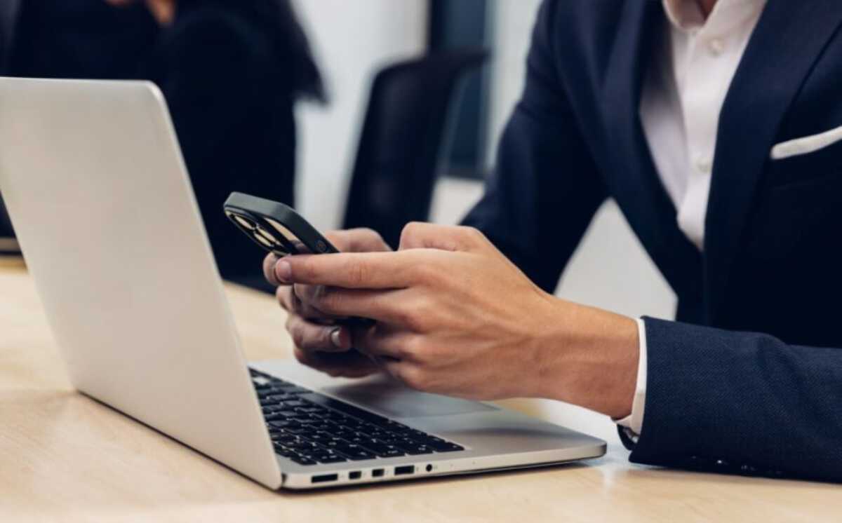 Mężczyzna w garniturze obsługuje telefon przed laptopem. Chat GPT dostępny na WhatsApp.